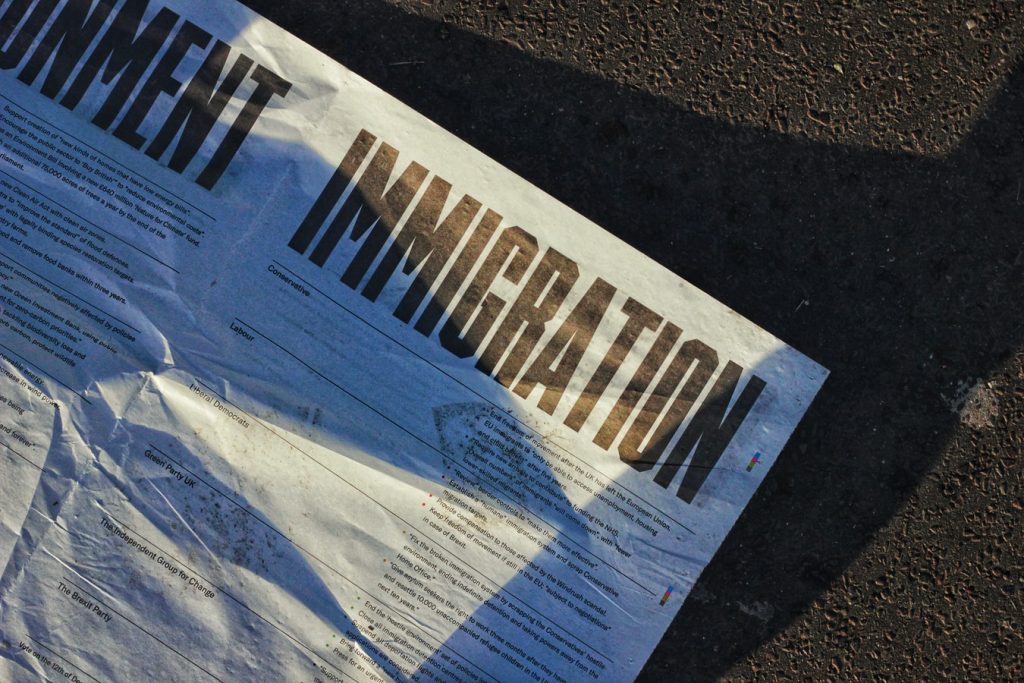 A photo of a newspaper on the ground, with the headline "Immigration" in large text.