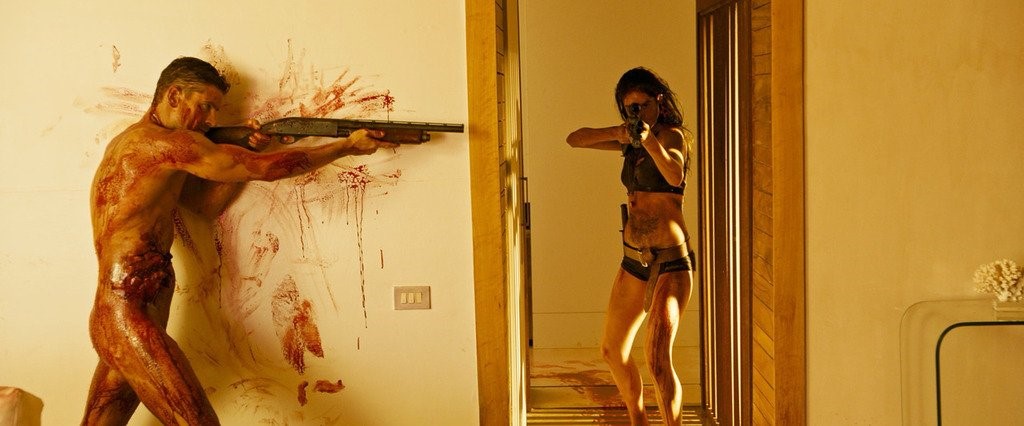 A still from film Revenge (Coralie Fargeat, 2017) showing a man and a woman with guns, both covered in blood.