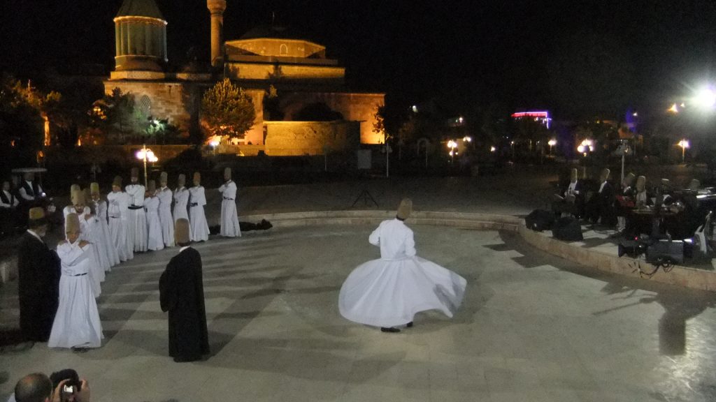 Start of Sama` at Rumi's mausoleum, photo by David Oughton. People in white costumes dance outside.