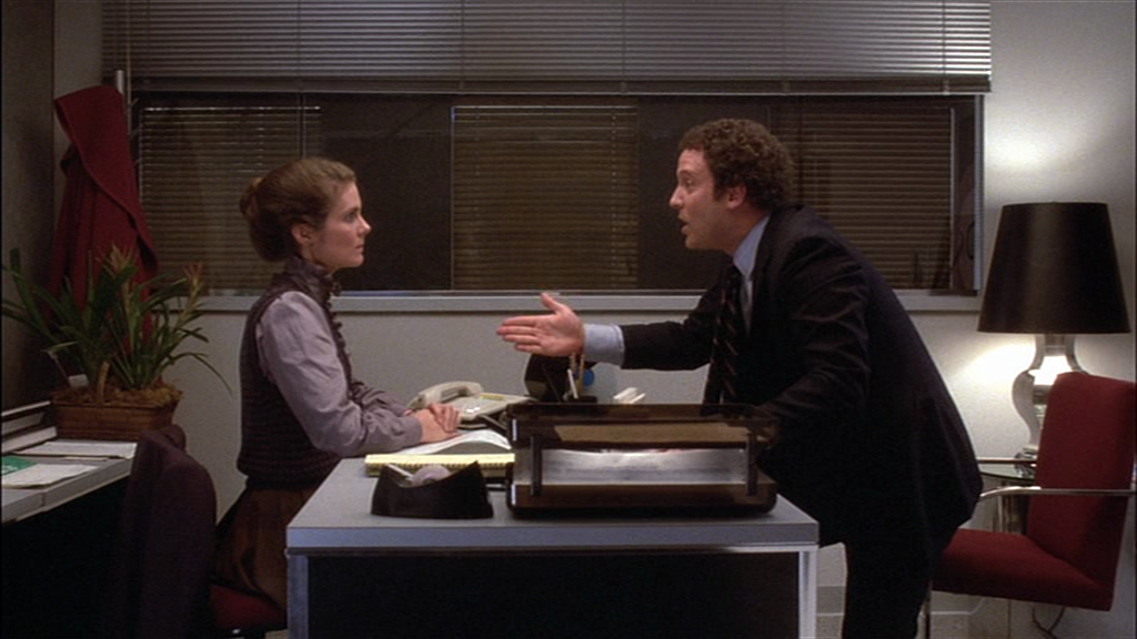 In an office setting, Albert Brooks acts opposite Julie Hagerty in a screenshot from film Lost in America (1985, dir. Albert Brooks, The Geffen Company).