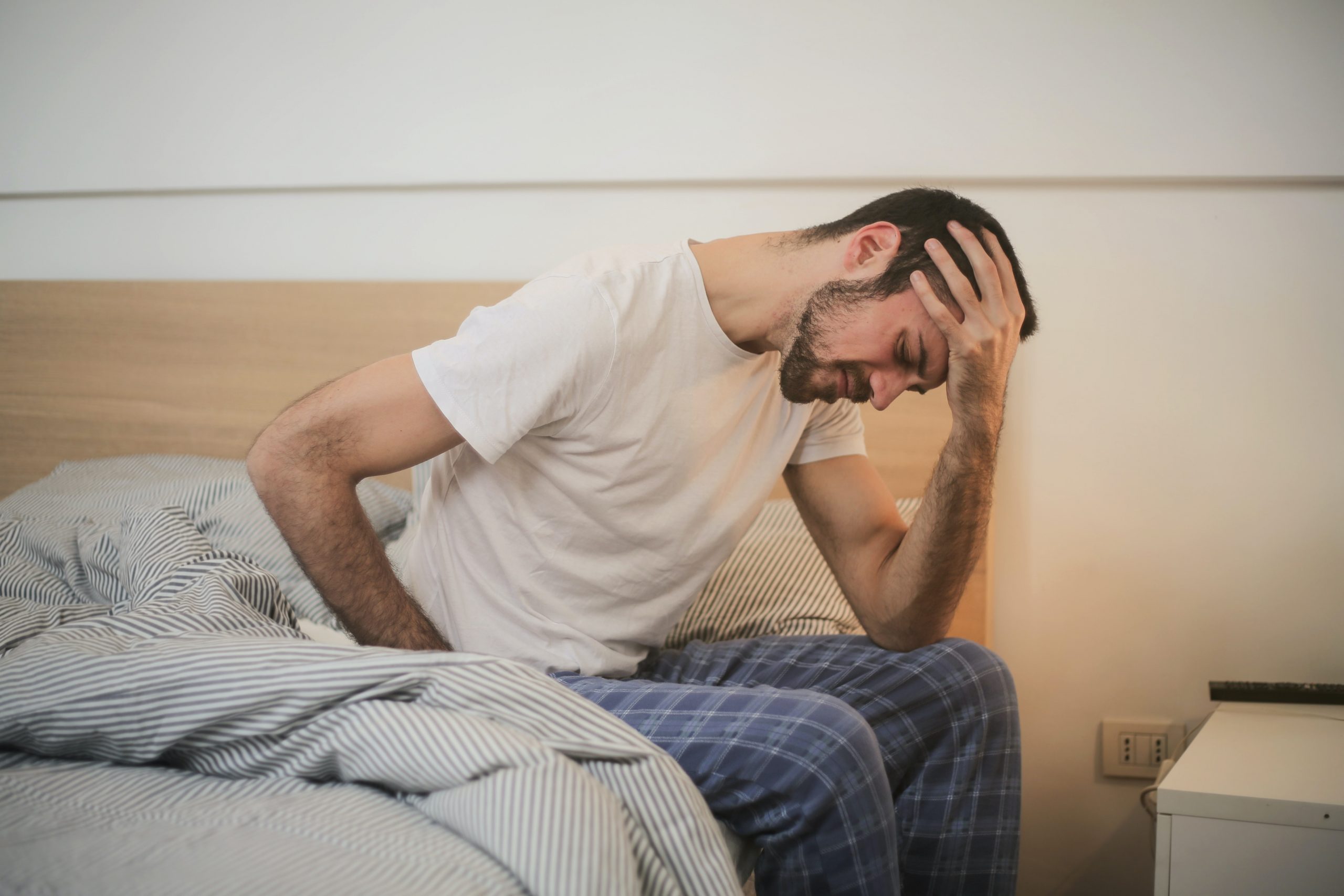 A man sits on the edge of a bed looking ashamed