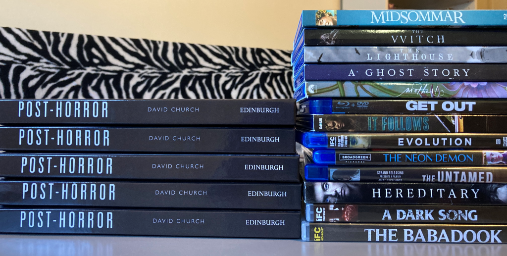 A photo of a stack of the book Post-Horror with some of David's post-horror film collection (a collection of blu-ray and dvds in a stack, including Midsommar, The VVitch, The Lighthouse and Hereditary).