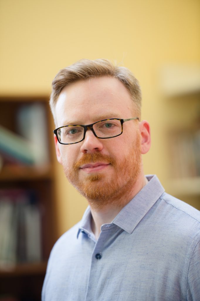 A photo of author David Martin-Jones, a white man with blond hair, glasses and a red beard, wearing a blue button-down shirt.