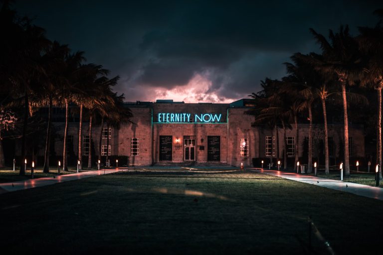 A photo of a building with the words "eternity now" in blue neon lights written over the door
