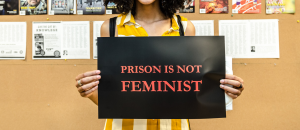 A faceless woman holds a sign that reads Prison Is Not Feminist