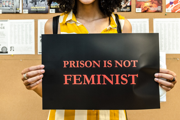 A faceless woman holds a sign that reads Prison Is Not Feminist