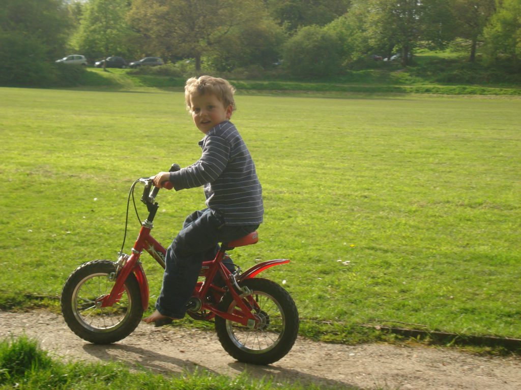 A child riding on a red bike along a footpath