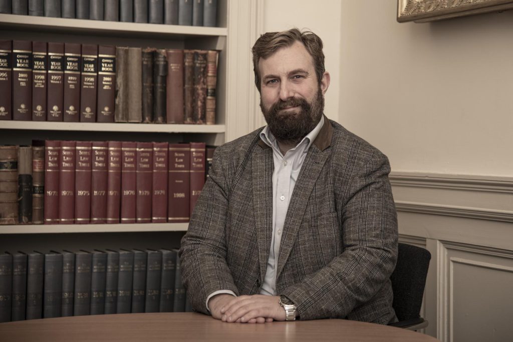 Portrait of Dr Jonny Hardman in front of a bookshelf