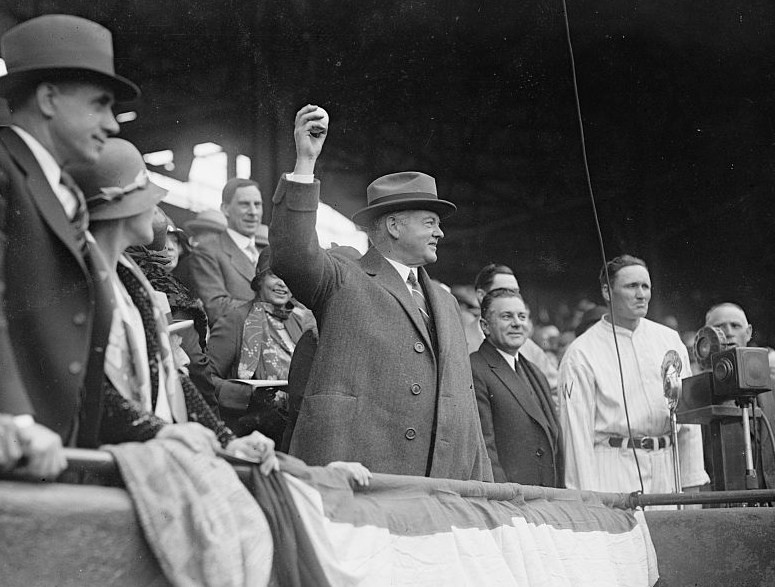 A black and white photo of Herbert Hoover holding up a baseball