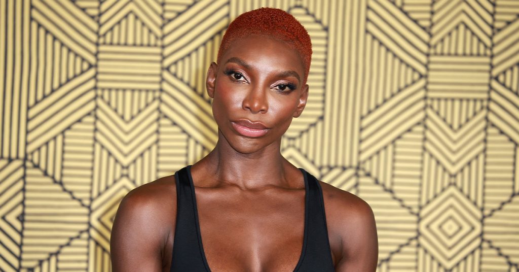A photo of actress Michaela Coel standing against a gold background