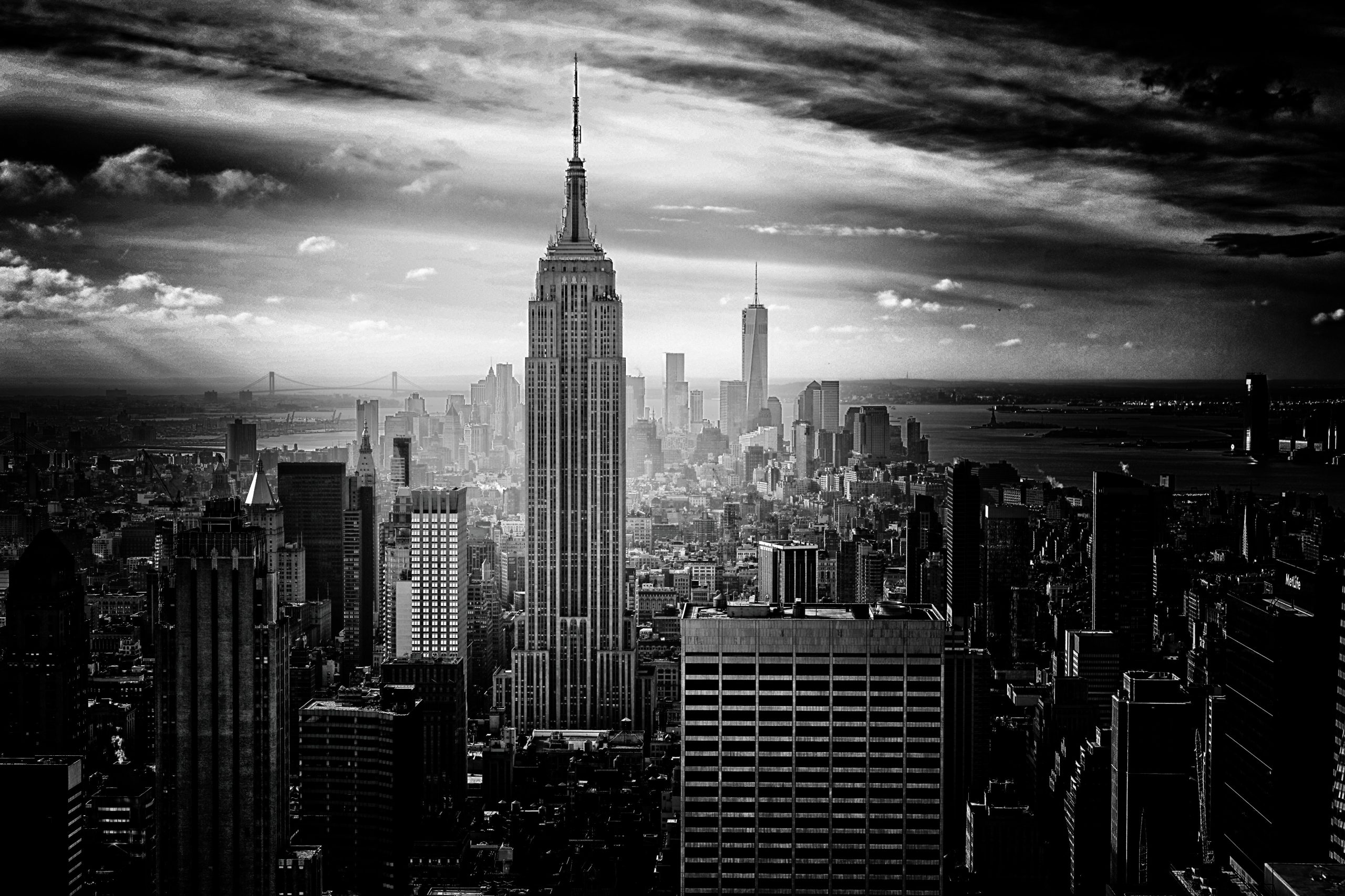 A black-and-white photograph cityscape of New York, centering on the Empire State Building, with dramatic cloulds above.