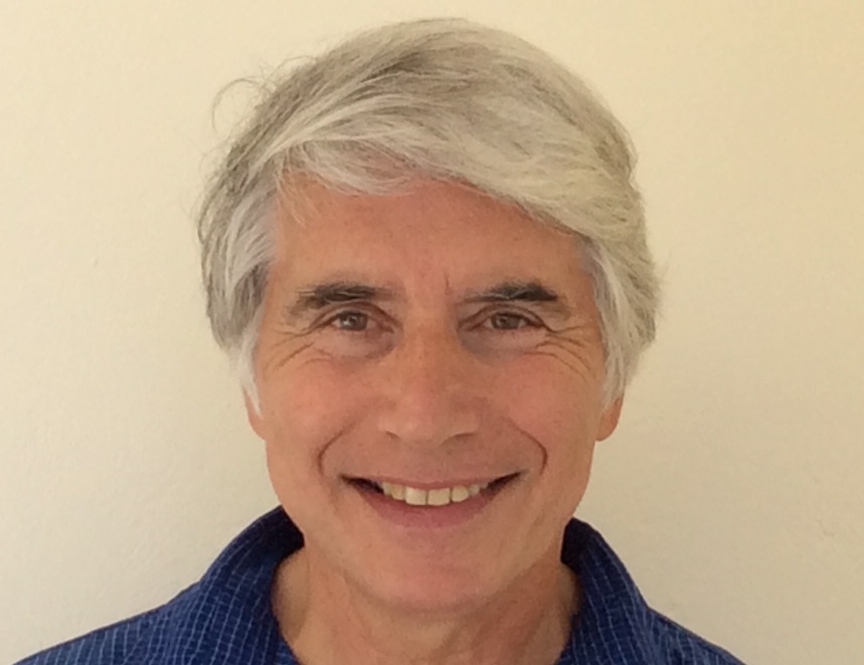A head shot picture of the author, Theodore Scaltsas. The author smiles at the camera wearing a sleeved blue shirt and he has light brown eyes and grey hair.