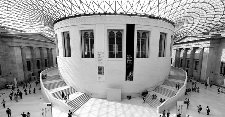A black and white image of a large museum gallery full of people