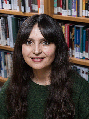 Ersev Ersoy smiles at the camera, with a bookcase in the background behind her