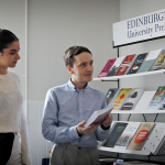 You can see four people in conversation, one holding a book, all standing in front of a book display with the banner 'Edinburgh University Press'. This is representative of EUP staff.