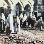 A group of Muslim women stand amongst the rubble of destroyed buildings