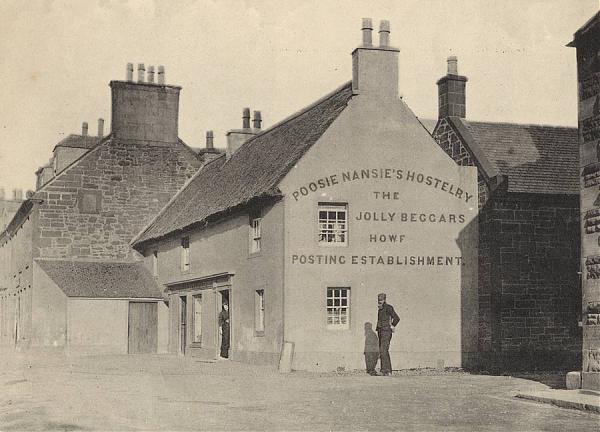 Black and white image showing the gable end of a house-like building with a figure standing in front of it. Text on the building reads 'Poosie Nansie's Hostelry and the Jolly Beggars Howf Posting Establishment'.