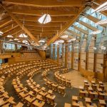 A large, open hall with rows of curved seating facing a stage. Most of the room is constructed from wood and glass.