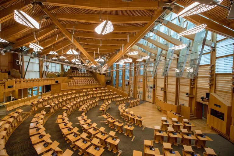 A large, open hall with rows of curved seating facing a stage. Most of the room is constructed from wood and glass.