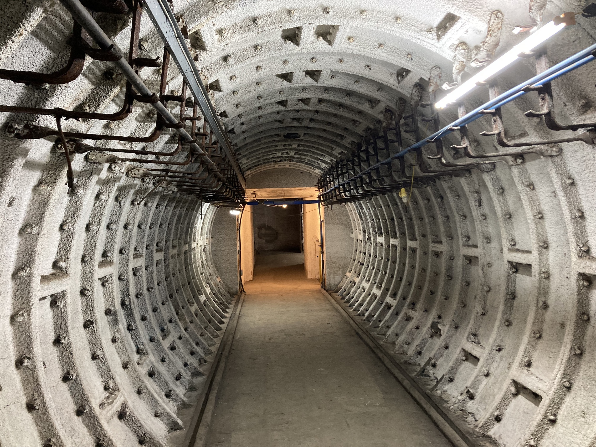 Looking down a round tunnel with strip lights and a small doorway at the far end.