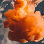 A cloud of orange liquid swirls against a dark background