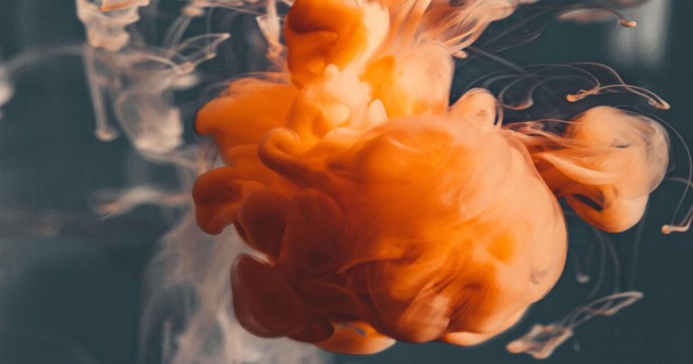 A cloud of orange liquid swirls against a dark background