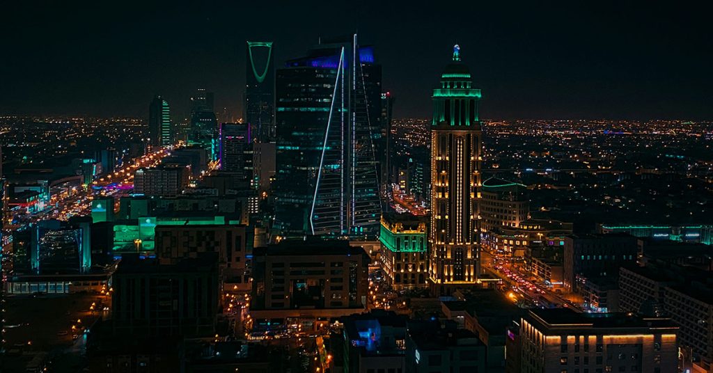 A photograph of Riyadh at night, with skyscrapers illuminated with colourful lighting