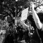 A black and white photograph of police in riot gear facing Black Lives Matter protestors