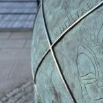 Close up image of a large blueish buoy, engraved with images of people preparing fish.