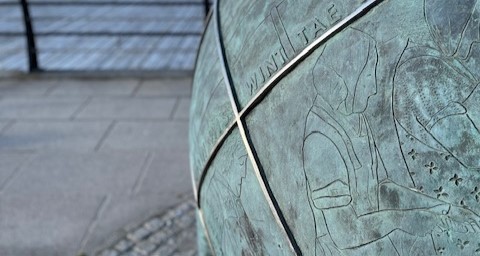 Close up image of a large blueish buoy, engraved with images of people preparing fish.