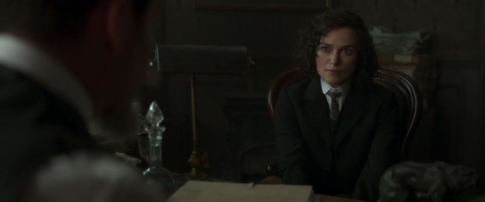 A woman dressed in a suit sits in a chair looking concerned