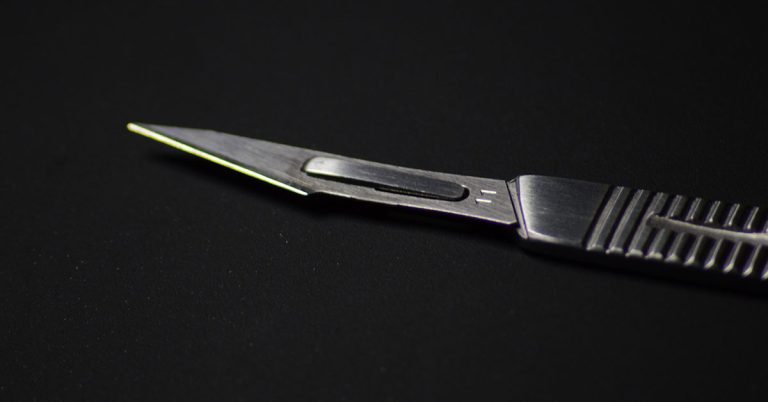 Photograph of a silver metal scalpel, taken from close-up, against a black background