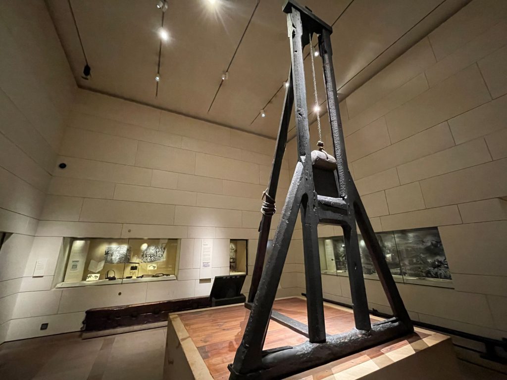 A guillotine-like device made of blackened wood, on display in an exhibition.