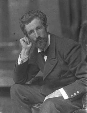 Black and white full- face photograph of R.B. Cunninghame Graham, seated in a pensive pose, with his right elbow resting on his right knee, his head tilted to the right and resting on his right hand and his left arm laid across his left leg.