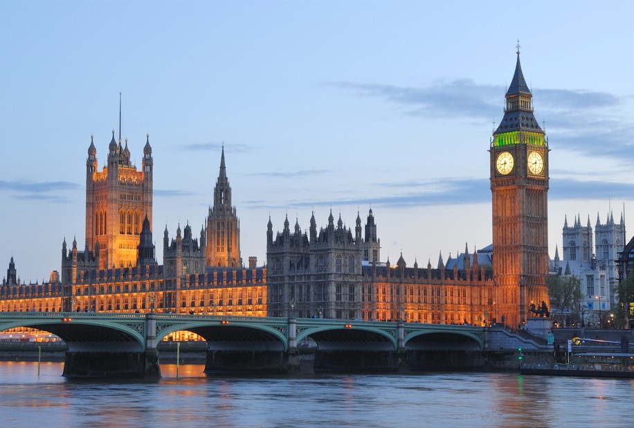 A landscape image of Big Ben and the House of Parliament lit up in a golden hue. The sky behind is light blue.