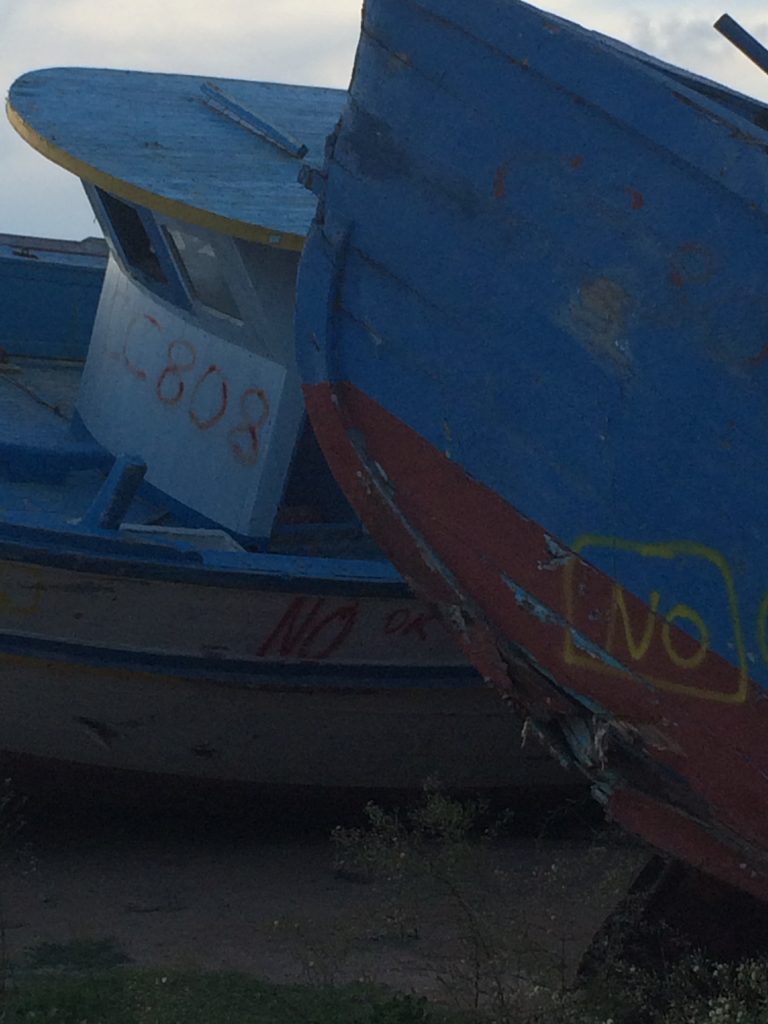 An image of a discarded wooden migrant boat with the word “no” graffitied on its side.