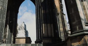 Stone statue viewed from behind beneath tall Gothic arches and dark stone columns, framing a bright blue sky with clouds