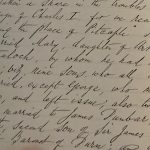 Close-up of a historical handwritten manuscript page in cursive ink, showing dense text on aged paper, held open by a person’s hand at the bottom edge.