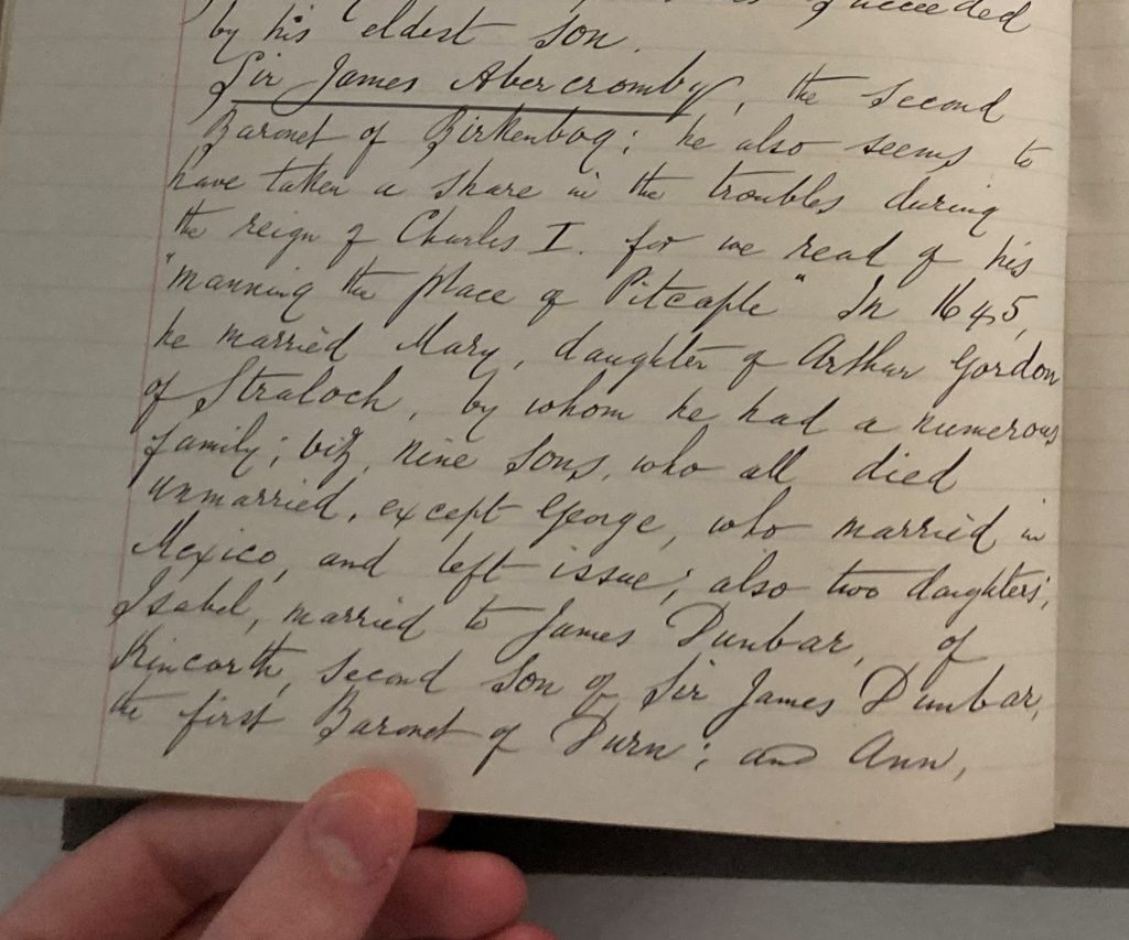 Close-up of a historical handwritten manuscript page in cursive ink, showing dense text on aged paper, held open by a person’s hand at the bottom edge.