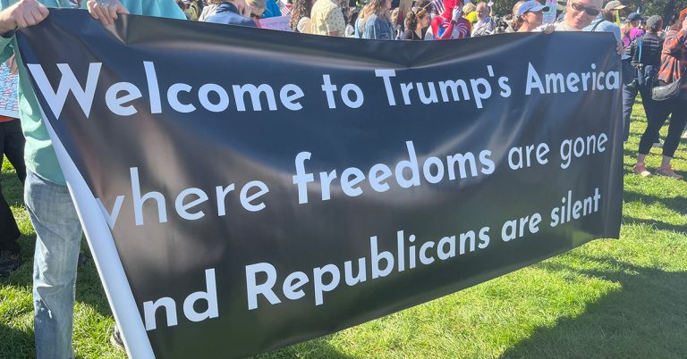 Protestors at a “No Kings” protest in Boston in 2025 hold up a sign, reading “Welcome to Trump’s America where freedoms are gone and Republicans are silent.”