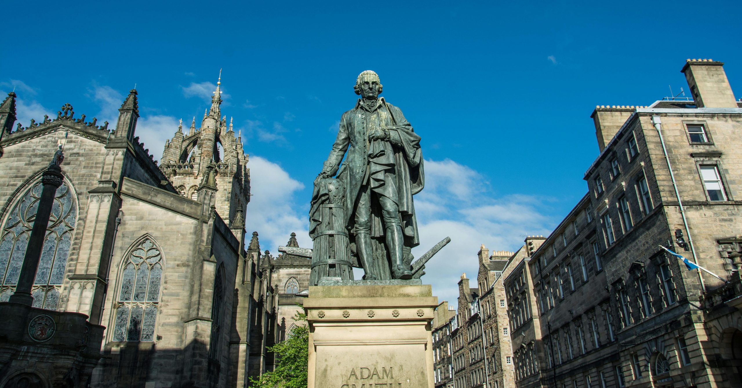 Statue of the philosopher and economist Adam Smith with St Giles’ Cathedral and other buildings in the background, against blue sky