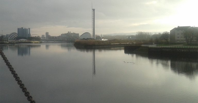 Looking out through the window of a former industrial building in Glasgow’s East End, we see large areas of derelict ex-industrial land in need of reclamation for development, and in the distance, other formerly industrial buildings.
