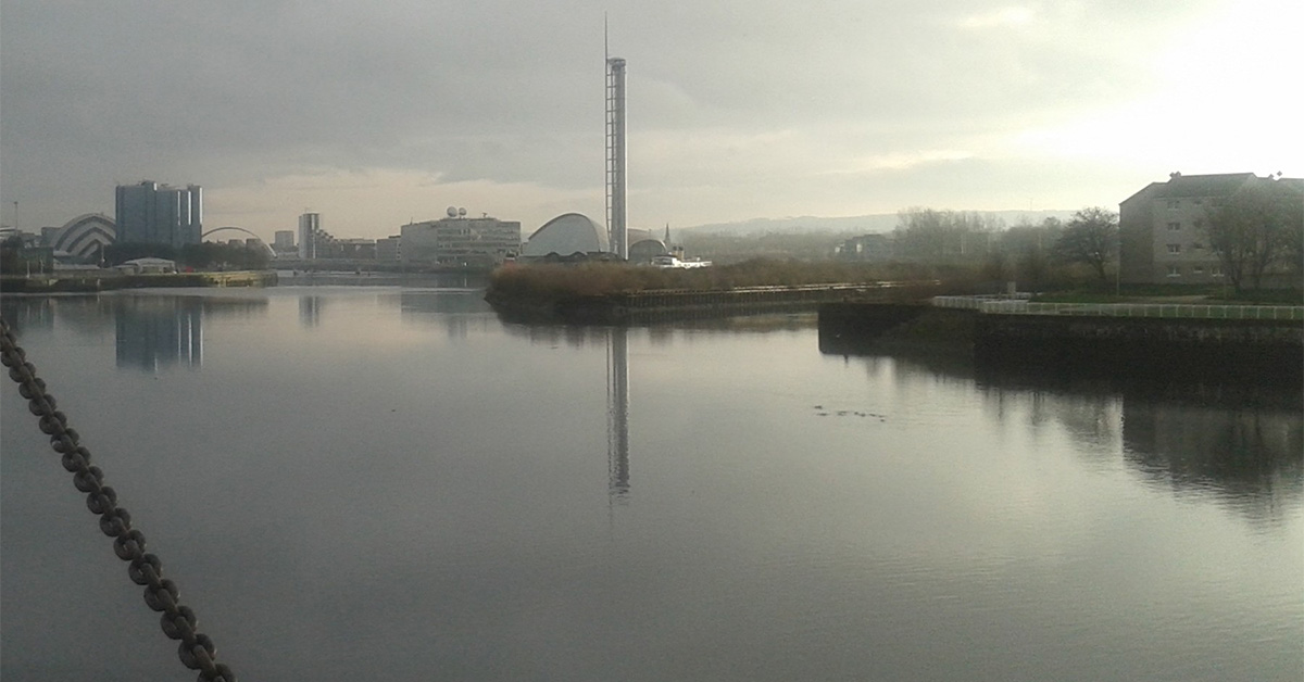 Looking out through the window of a former industrial building in Glasgow’s East End, we see large areas of derelict ex-industrial land in need of reclamation for development, and in the distance, other formerly industrial buildings.
